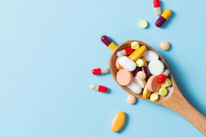 A spoon filled with multiple pills and vitamins, overflowing beyond it.