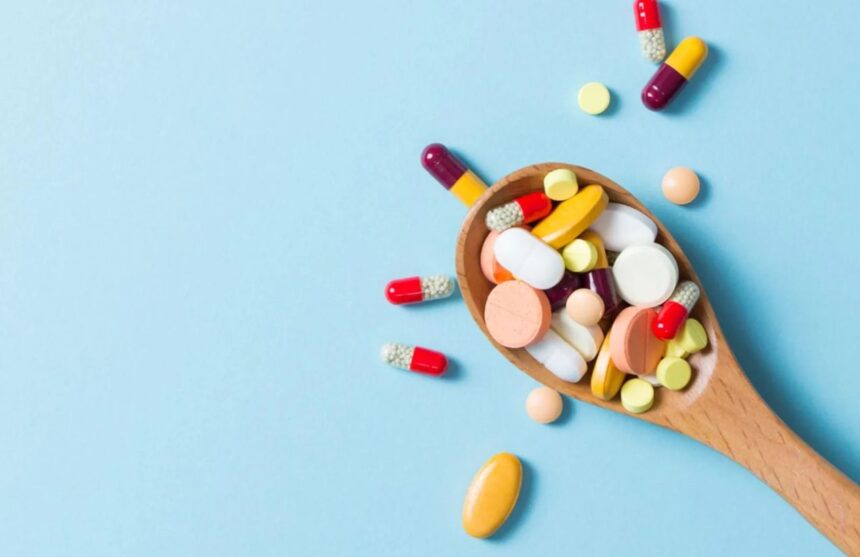 A spoon filled with multiple pills and vitamins, overflowing beyond it.