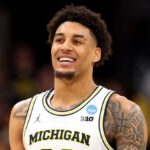The young Michigan player smiling during a game, with his large afro and white uniform