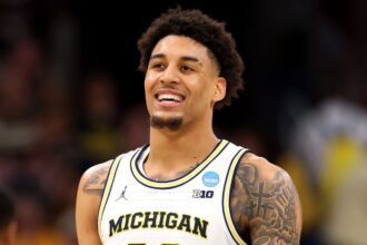 The young Michigan player smiling during a game, with his large afro and white uniform