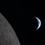 A historic photo of the Moon with a completely black background and planet Earth visible behind it.