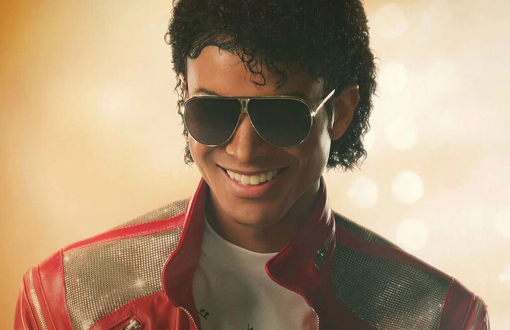 Michael Jackson smiling at his audience wearing his iconic red jacket and large sunglasses.