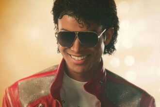 Michael Jackson smiling at his audience wearing his iconic red jacket and large sunglasses.