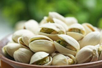 A bowl on a table filled with pistachios ready to eat.