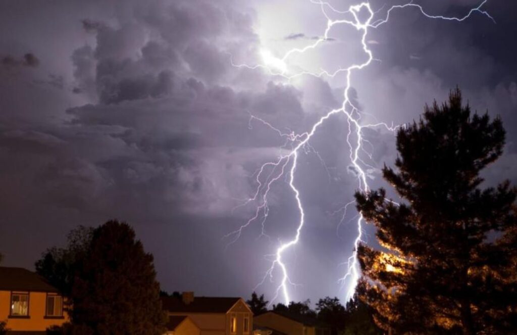 Lightning striking down from the sky toward some houses.