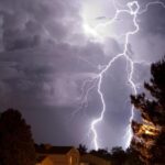 Lightning striking down from the sky toward some houses.