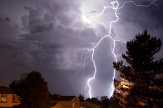 Lightning striking down from the sky toward some houses.
