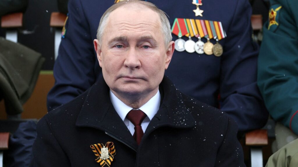 Vladimir Putin watching a military spectacle alongside his circle of government leaders in the stands.