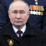 Vladimir Putin watching a military spectacle alongside his circle of government leaders in the stands.