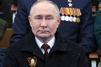 Vladimir Putin watching a military spectacle alongside his circle of government leaders in the stands.
