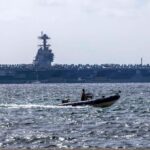 An aircraft carrier on the horizon, awaiting orders at sea.