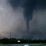 A dangerous tornado crossing a state highway in Oklahoma with several cars nearby.