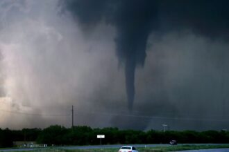 A dangerous tornado crossing a state highway in Oklahoma with several cars nearby.