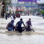 A flooded street in Afghanistan with several people helping each other recover their belongings