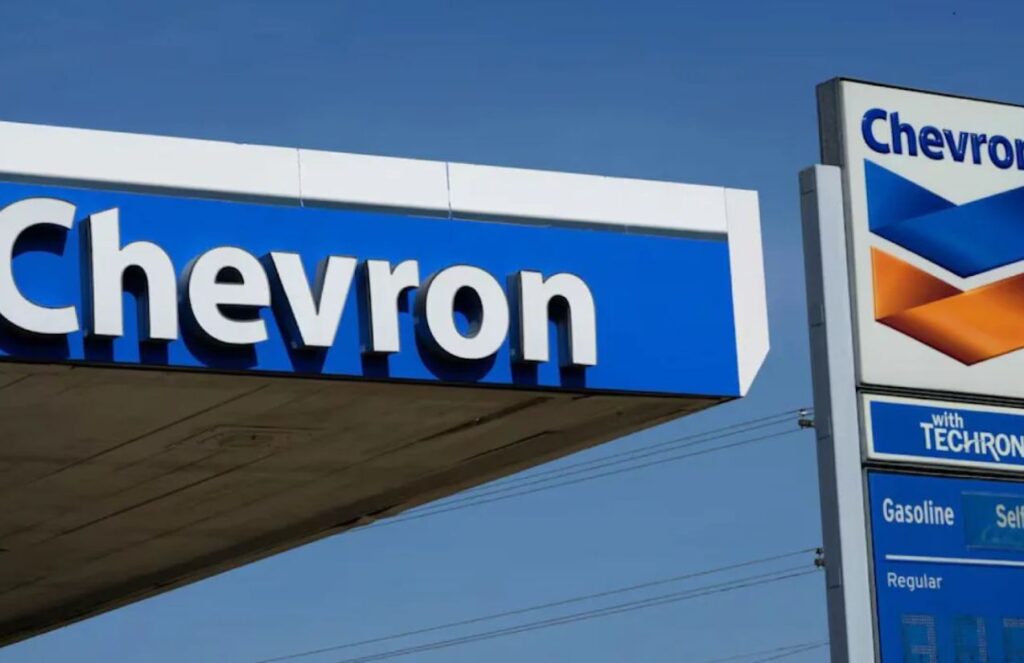 Two Chevron signs on the street with a gas station in the background.