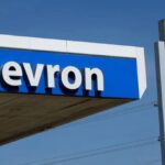 Two Chevron signs on the street with a gas station in the background.