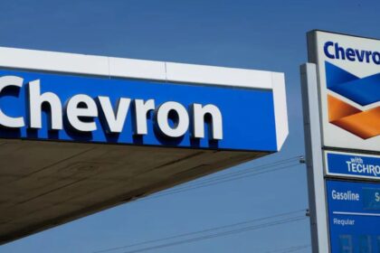 Two Chevron signs on the street with a gas station in the background.