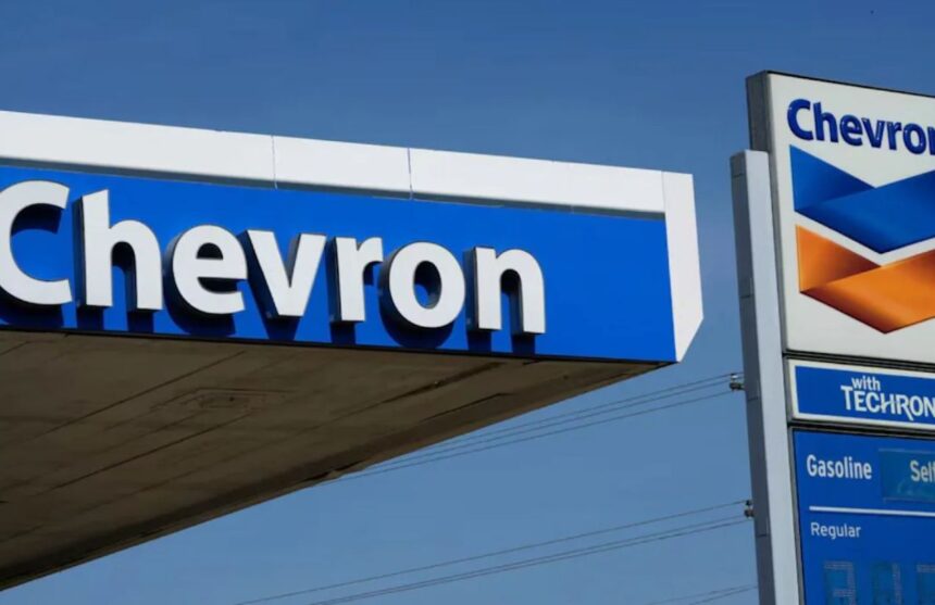 Two Chevron signs on the street with a gas station in the background.