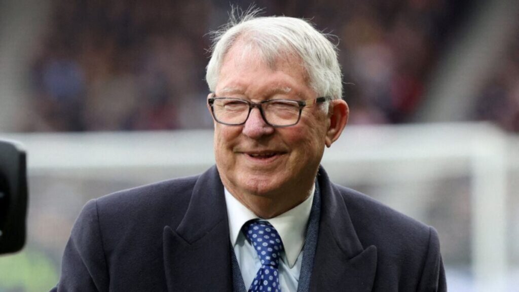 Alex Ferguson on a football field, happy and smiling brightly while enjoying the moment.