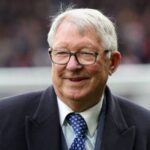 Alex Ferguson on a football field, happy and smiling brightly while enjoying the moment.