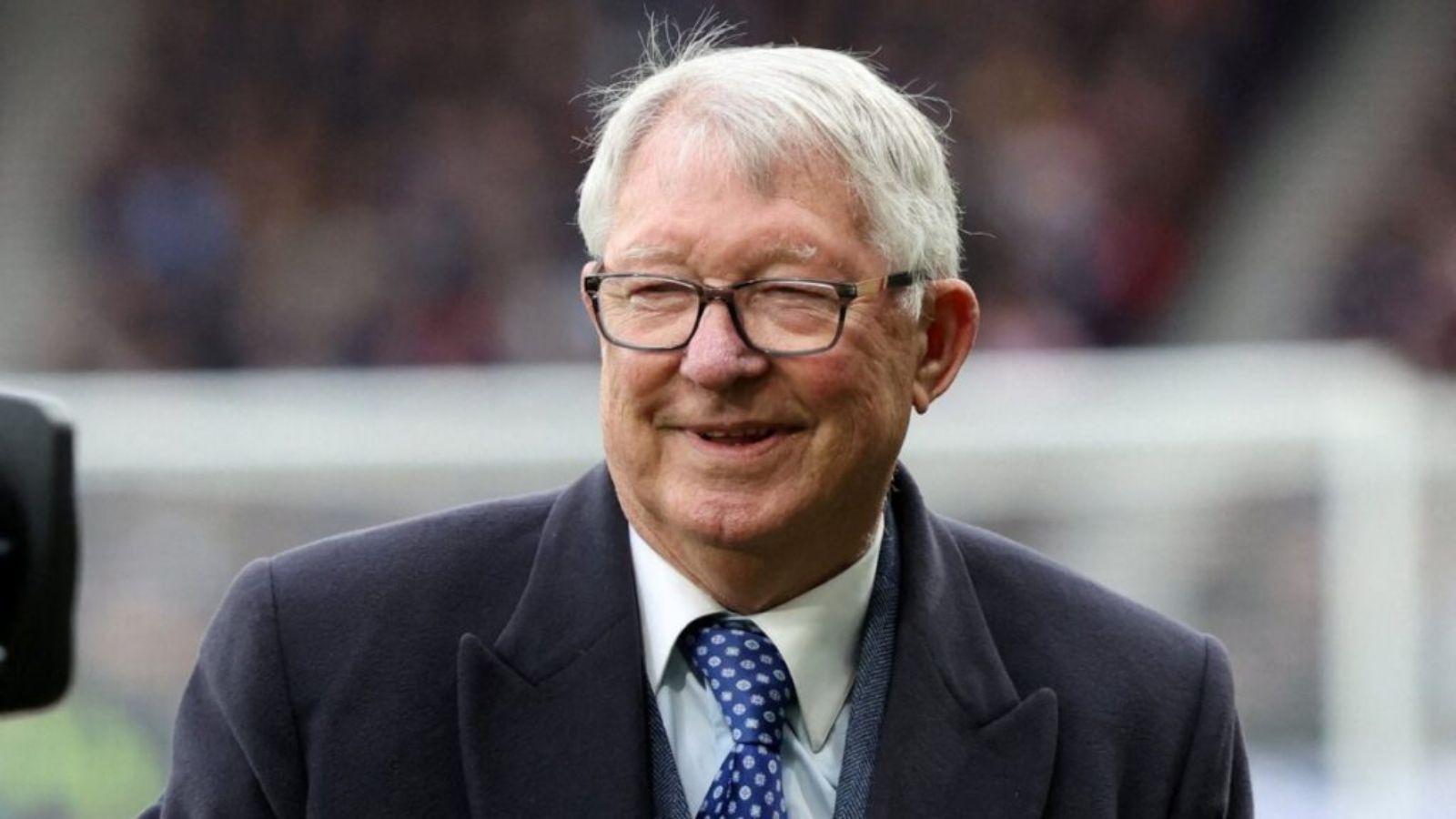 Alex Ferguson on a football field, happy and smiling brightly while enjoying the moment.