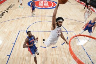 Jarrett Allen of the Cleveland Cavaliers making a dunk while two Detroit Pistons players watch him rise into the air.