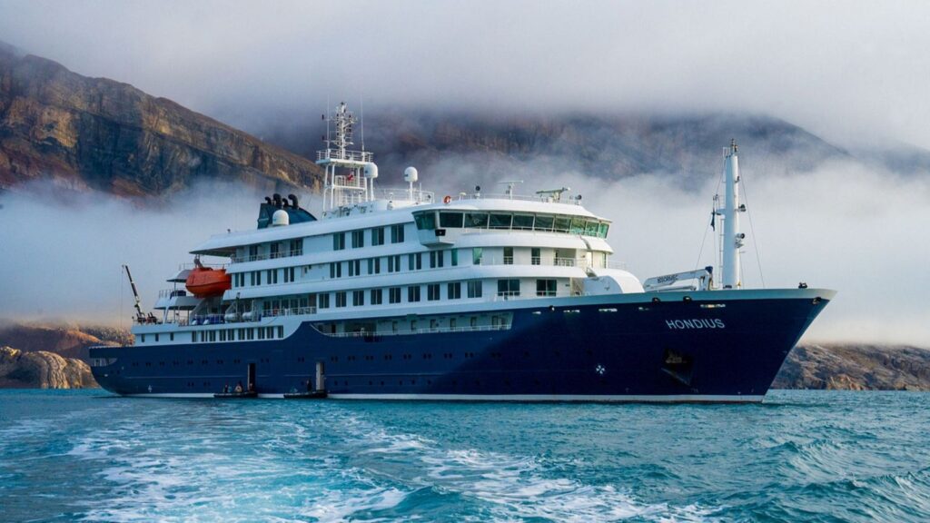 The now-famous blue cruise ship in the middle of the sea with a mountainous landscape in the background.