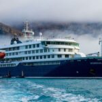 The now-famous blue cruise ship in the middle of the sea with a mountainous landscape in the background.