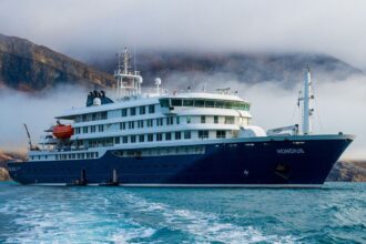 The now-famous blue cruise ship in the middle of the sea with a mountainous landscape in the background.