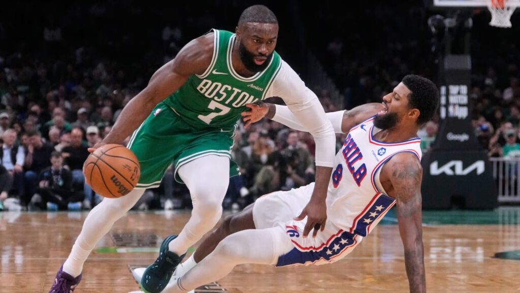 A matchup between players from both teams where one is dribbling and the other is falling to the floor.