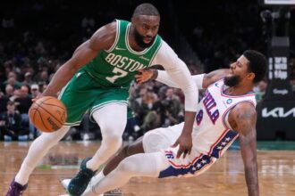 A matchup between players from both teams where one is dribbling and the other is falling to the floor.