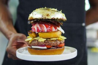 A person holding a gold-covered hamburger.