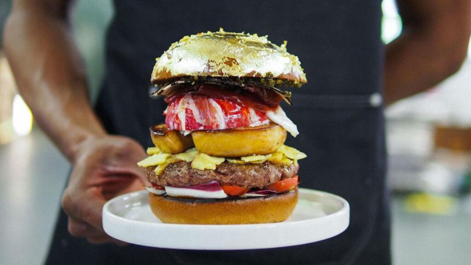A person holding a gold-covered hamburger.