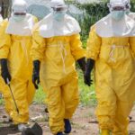 Four people wearing yellow protective suits spraying liquid on the streets to prevent the spread of Ebola.
