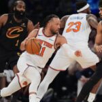 Jalen Brunson dribbling past several Cleveland Cavaliers players while maintaining possession of the ball to attack the basket.