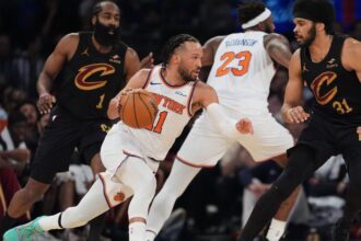 Jalen Brunson dribbling past several Cleveland Cavaliers players while maintaining possession of the ball to attack the basket.