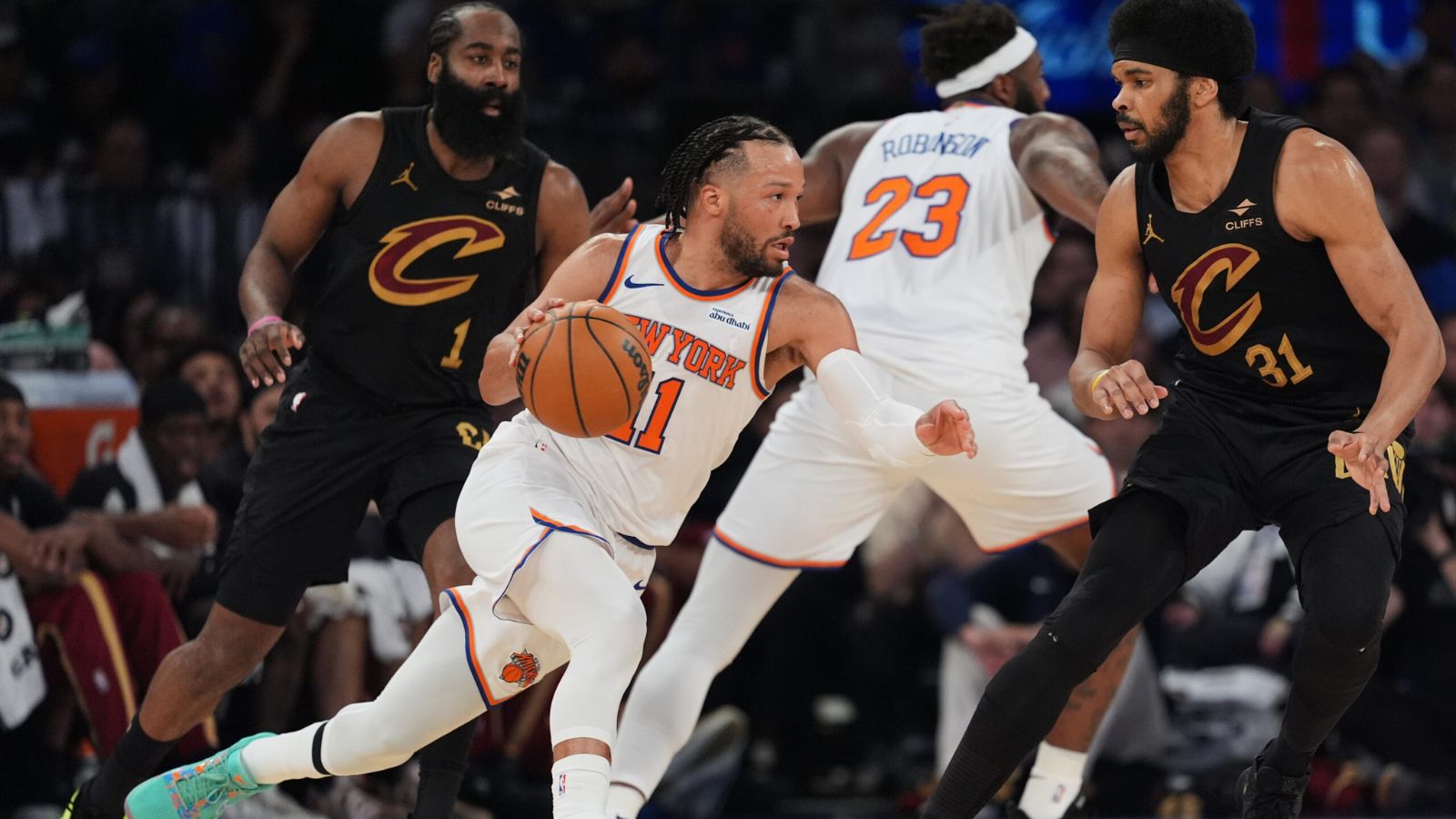 Jalen Brunson dribbling past several Cleveland Cavaliers players while maintaining possession of the ball to attack the basket.