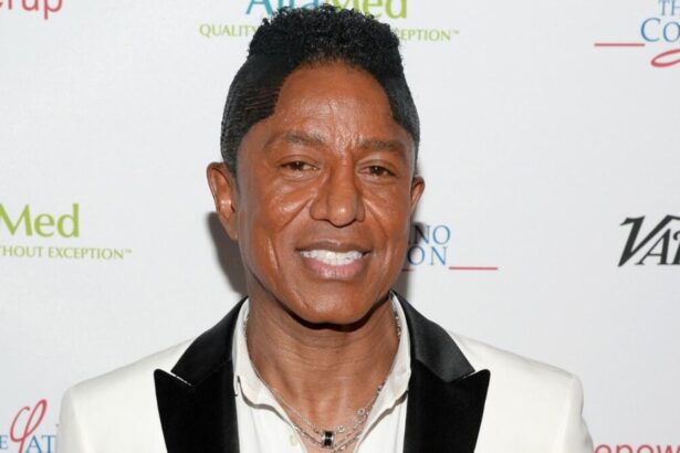 Jermaine Jackson smiling on a red carpet with a big smile and an elegant suit.