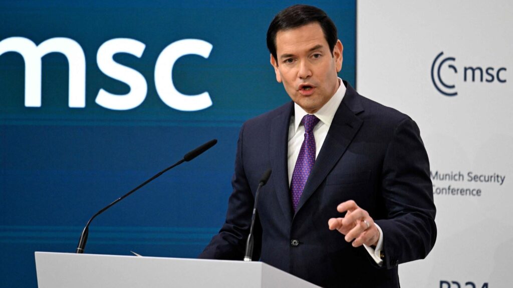 Marco Rubio giving a speech in an elegant suit with a large audience in the room.