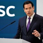 Marco Rubio giving a speech in an elegant suit with a large audience in the room.