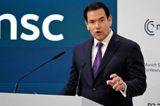Marco Rubio giving a speech in an elegant suit with a large audience in the room.