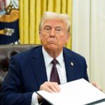Donald Trump sitting in his office while reviewing some physical documents.