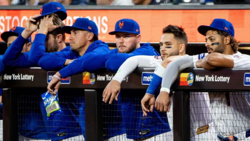 Several New York Mets players with sad expressions in the bullpen after the team’s losses.