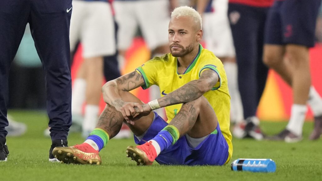Neymar sitting on the grass of the field after finishing a match that he lost.
