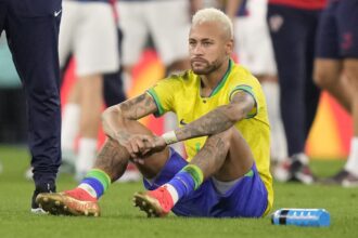 Neymar sitting on the grass of the field after finishing a match that he lost.