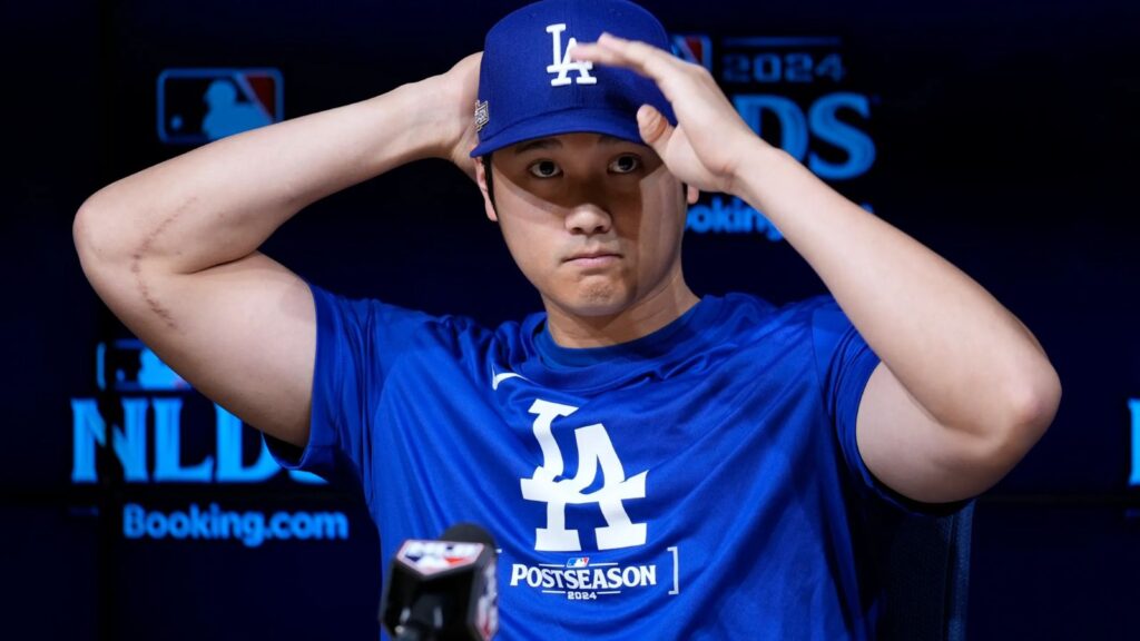 Shohei Ohtani at a press conference adjusting his cap with a slightly sad or aggressive expression.
