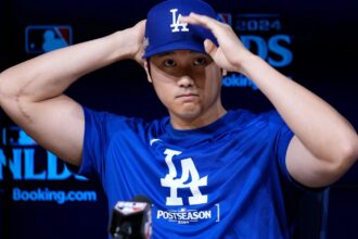 Shohei Ohtani at a press conference adjusting his cap with a slightly sad or aggressive expression.