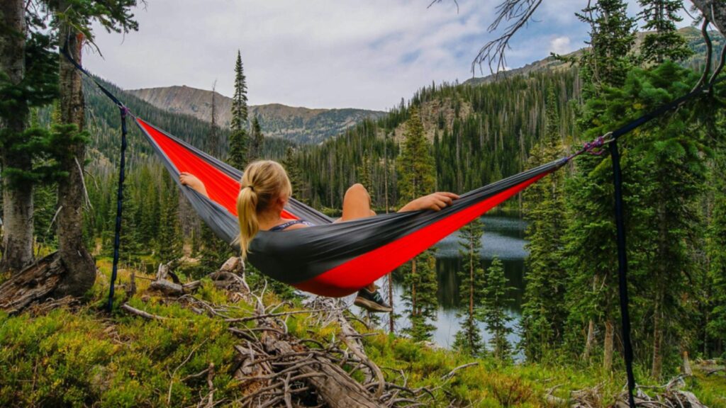Short vacations could be the new solution to stress, according to a recent study A woman sitting in a hammock tied between two trees while overlooking a landscape filled with nature.