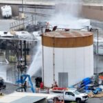 A large tank filled with chemicals being sprayed with water or another liquid to prevent the gas from spreading rapidly.