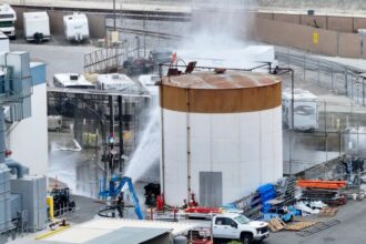 A large tank filled with chemicals being sprayed with water or another liquid to prevent the gas from spreading rapidly.